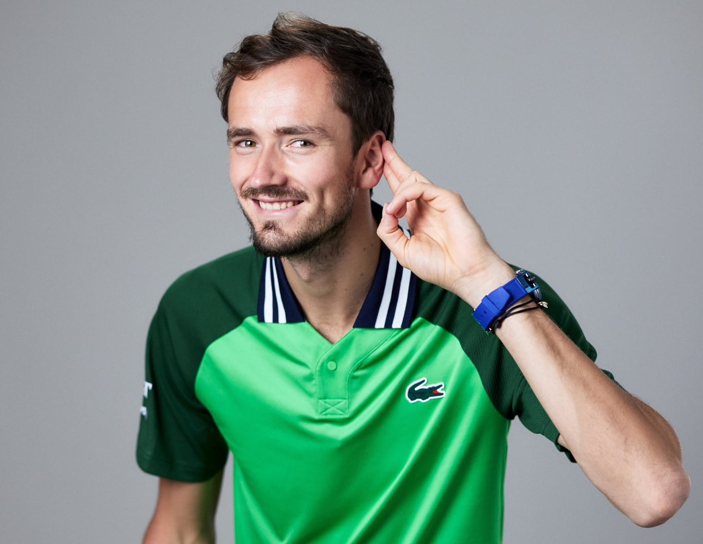 Daniil Medvedev sonriendo y haciendo un gesto de escucha durante una sesión de fotos oficial de Lacoste.