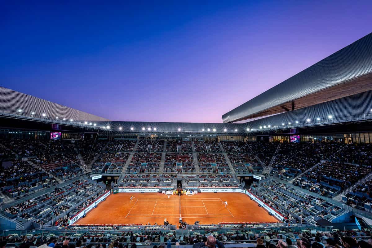 Panorámica nocturna de la pista central de la Caja Mágica durante el Mutua Madrid Open 2026, con las luces encendidas y la arcilla roja en primer plano.