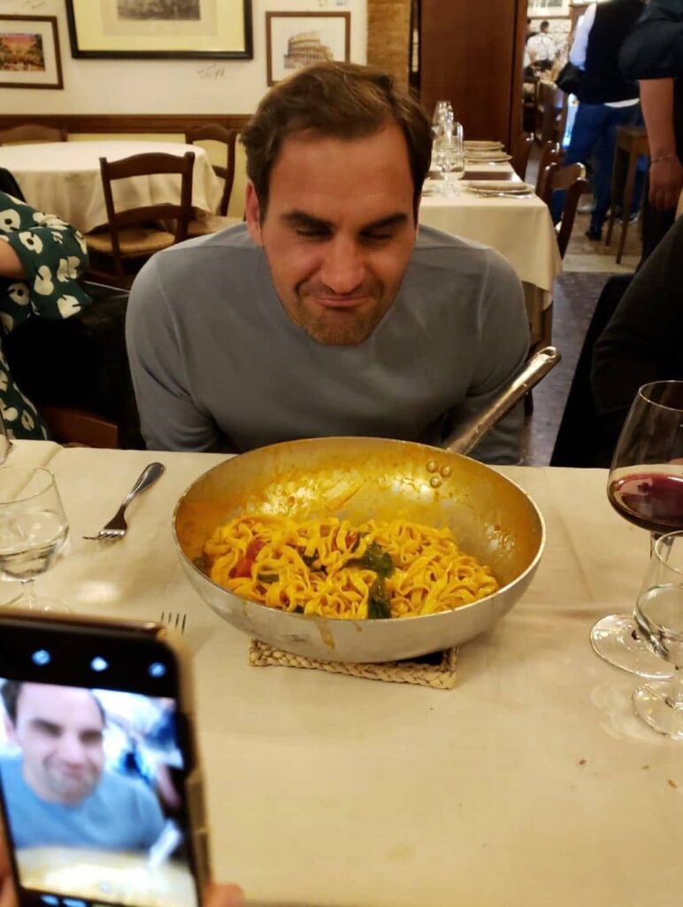 Roger Federer con los ojos cerrados, disfrutando del aroma de una sartén de pasta italiana recién preparada durante una cena de gala.