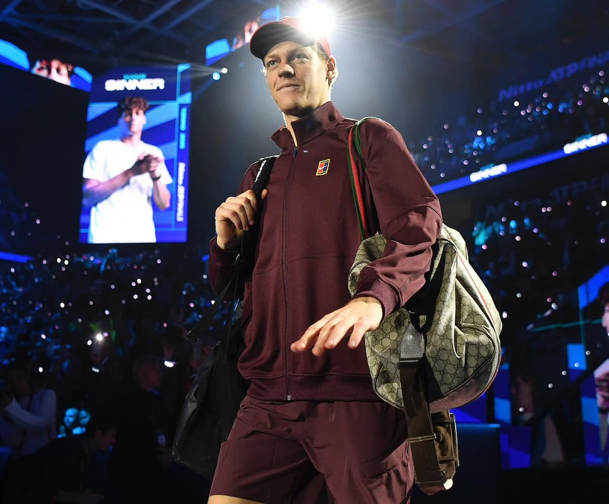 Jannik Sinner caminando hacia la pista con su bolso Gucci monogramado y conjunto técnico Adidas en un torneo ATP.