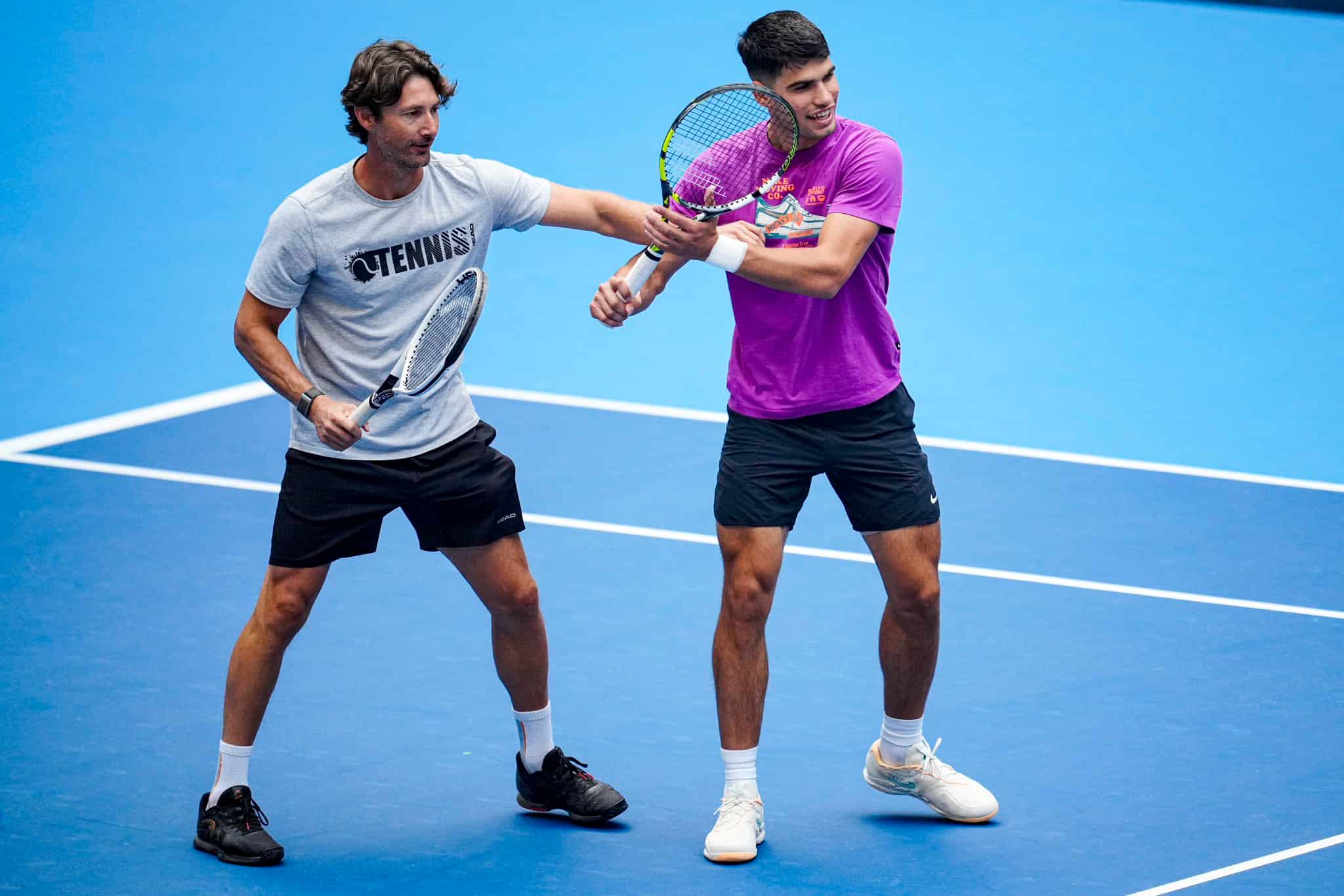 Juan Carlos Ferrero ajustando la técnica del brazo de Carlos Alcaraz durante un entrenamiento, capturando la esencia de su relación de entrenador y pupilo que Ferrero confiesa que no podría rechazar retomar.