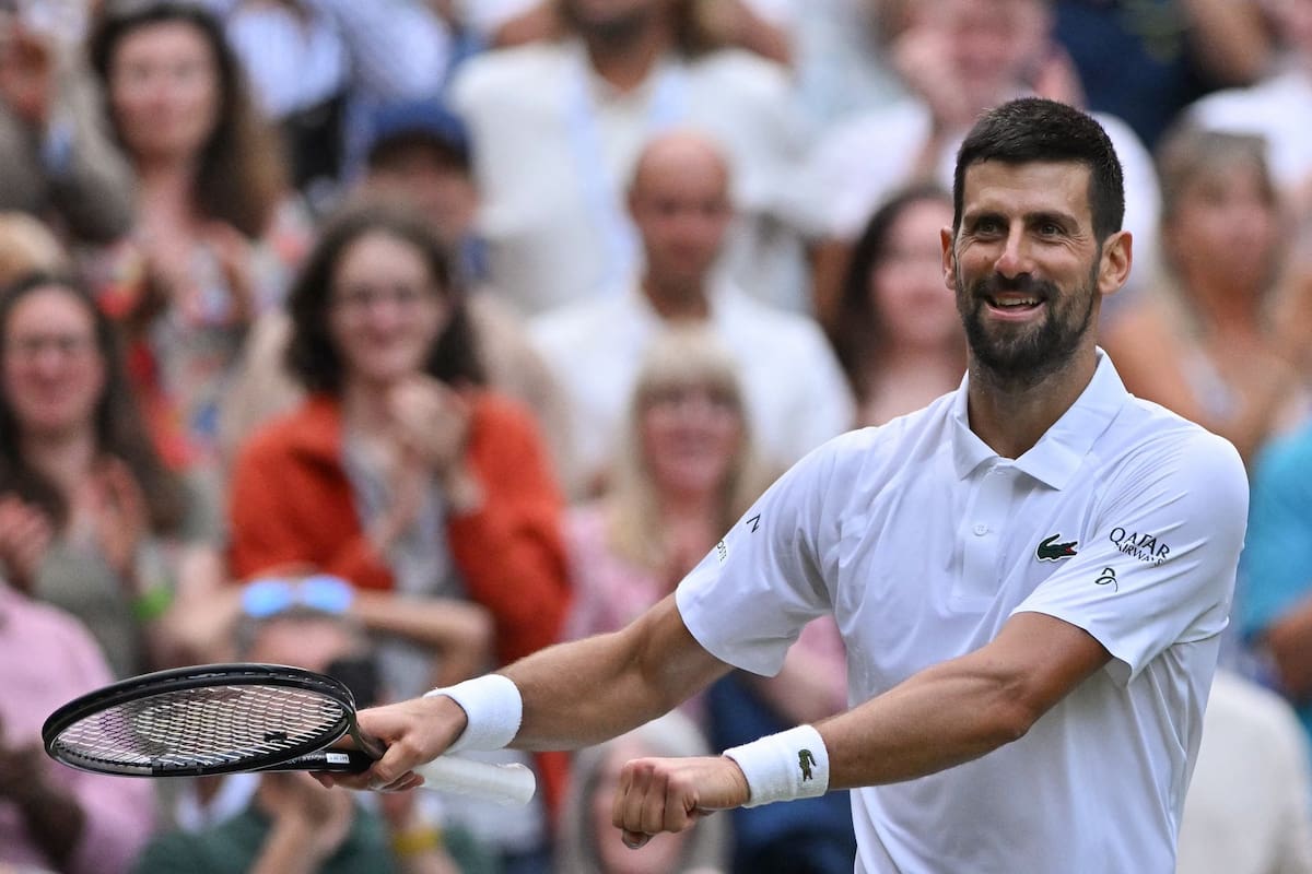 Novak Djokovic sonriendo y celebrando un punto con el puño cerrado frente a una multitud en las gradas.